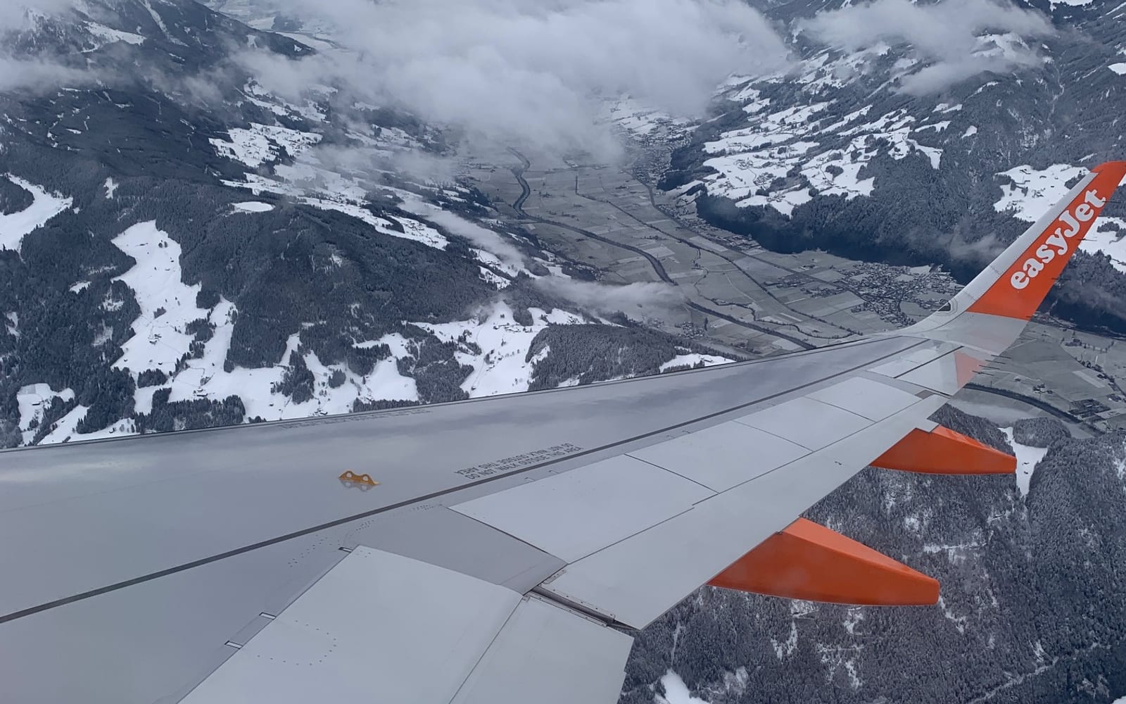 View from an aircraft over a snow-covered mountain valley beneath low cloud.