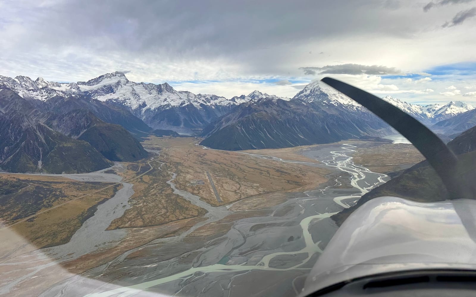 View from a light aircraft over a braided mountain valley with snow-covered peaks ahead.